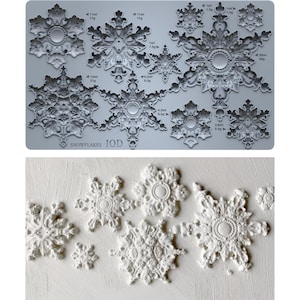 May include: A silicone mold sheet labeled SNOWFLAKES IOD featuring various intricate snowflake designs with volume and weight measurements in ml and grams, alongside a set of white molded snowflake shapes with ornate details.