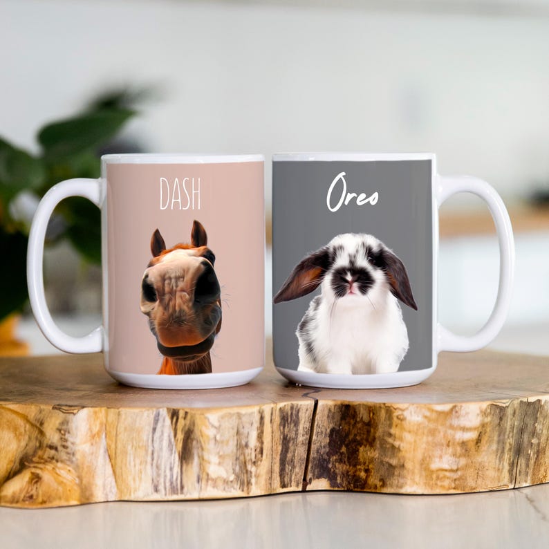 K&ouml;nnte beinhalten: Zwei wei&szlig;e Keramikbecher. Ein Becher zeigt ein Pferdgesicht mit dem Namen "Dash" dar&uuml;ber. Der andere Becher hat ein schwarz-wei&szlig;es Kaninchengesicht mit dem Namen "Oreo" dar&uuml;ber. Beide Becher haben einen wei&szlig;en Griff und stehen auf einer Holzoberfl&auml;che.
