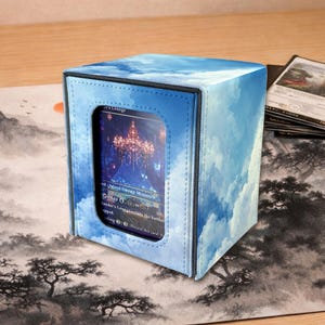 May include: A blue card storage box with a cloud pattern. The box has a clear window displaying a card with a fantasy landscape. The box is on a wooden surface with a landscape-themed playmat.