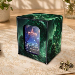 Könnte beinhalten: Eine quadratische Deck-Box mit einem dunkelgrünen, spektralen Totenkopf-Grafikdruck. Die Vorderseite hat einen rechteckigen Ausschnitt, der eine Sammelkarte mit einer Kronleuchter-Illustration und dem Text Island Swamp Mountain zeigt.
