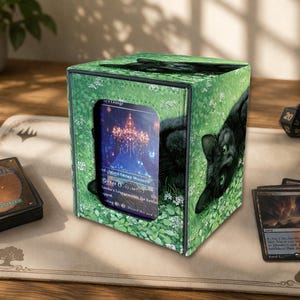 May include: Green card storage box featuring a black cat design on a grassy background. The box has a clear window displaying a card with a chandelier image. A deck of cards and dice are visible.
