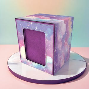 May include: A square box with a celestial design featuring purple, blue, and pink clouds and stars. The box has a rectangular opening with a purple interior. The box is on a white and purple circular stand.