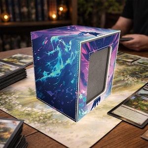 Peut inclure: Une boîte de rangement de cartes en forme de cube avec un design abstrait vibrant dans les tons de bleu, de violet et de turquoise. La boîte présente une bordure cousue blanche et une ouverture rectangulaire. La boîte est posée sur un tapis de jeu avec des cartes.
