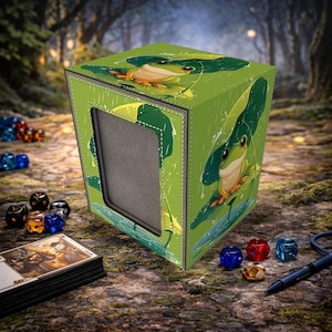 Könnte beinhalten: Grüne und beige Kartenaufbewahrungsbox mit einem Frosch- und Blattdesign. Die Box hat ein Fenster und ist von Würfeln, Karten und einem Stift umgeben. Die Box besteht aus einem strukturierten Material mit einer genähten Umrandung.