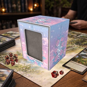 May include: A pastel-colored card storage box with a floral, skull, and sword design. The box has a window and is surrounded by playing cards and dice. The color scheme includes pink, blue, and white.