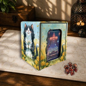 May include: A card storage box with a whimsical cat illustration. The box is open, revealing a card with a colorful image. The cat is black and white, holding flowers, surrounded by yellow dandelions. The box is on a patterned surface.
