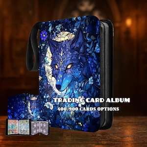 May include: A blue trading card album with a wolf design. The cover features a detailed illustration of a wolf's face with glowing yellow eyes, surrounded by floral elements. The text "TRADING CARD ALBUM" and "400/900 CARDS OPTIONS" are visible.