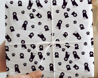 May include: A wrapped gift box featuring a white background with a repeating pattern of black dog illustrations and paw prints. The box is tied with white twine. The overall theme is related to pets and gifts.