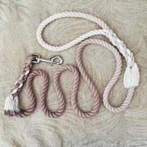 May include: A pink and white cotton rope dog leash with a silver clip. The leash is made of two ropes, one pink and one white, that are braided together.