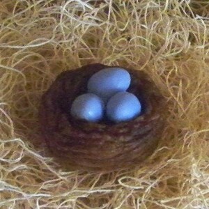Op de afbeelding: Een klein bruin gevlochten vogelnest met drie lichtblauwe eieren erin.