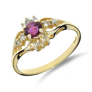 Puede incluir: Un anillo de oro con una piedra preciosa púrpura rodeada de piedras blancas más pequeñas. El anillo tiene un diseño delicado e intrincado.