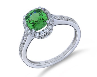 May include: A silver ring featuring a green gemstone encircled by a halo of smaller diamonds. The band is also set with diamonds. The ring is engraved with "128 - D028 750 925".