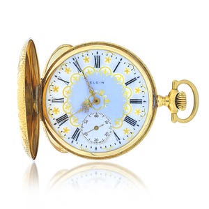 May include: A gold Elgin pocket watch with an open face, featuring a light blue and white dial with black Roman numerals and gold floral details. The watch has a small seconds dial and a decorative gold case.