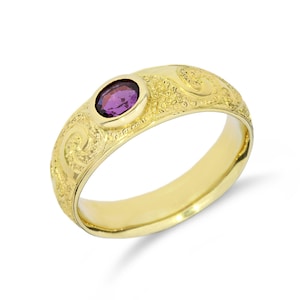Puede incluir: Un anillo de oro con una piedra preciosa ovalada de color púrpura. El anillo tiene un diseño floral grabado y un acabado pulido. La piedra preciosa está engastada en un bisel. Una joya clásica.