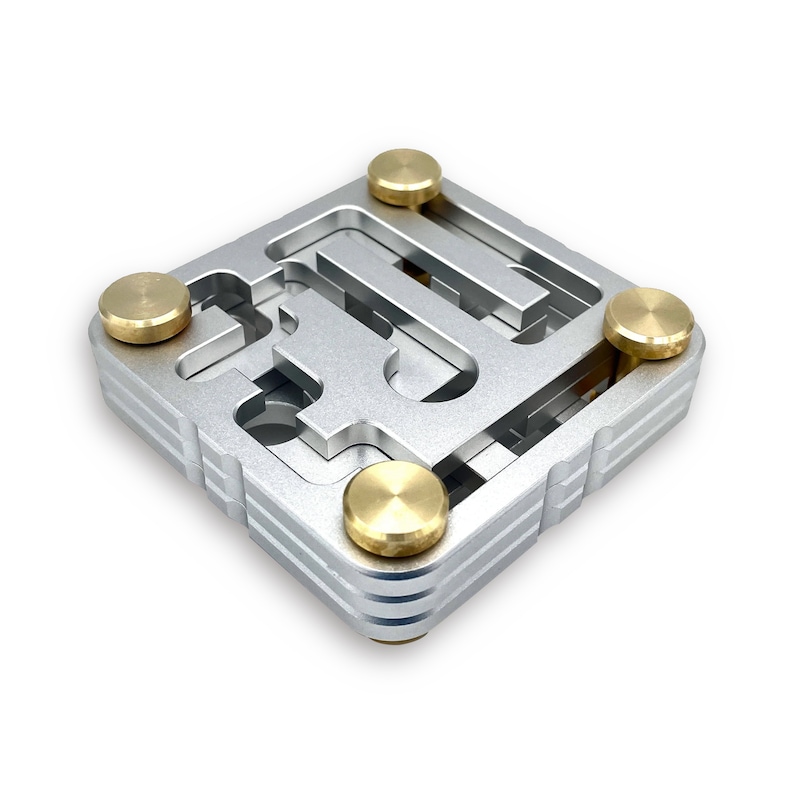 May include: A silver metal maze puzzle with four brass-colored knobs. The puzzle has a square shape with a complex internal track design. The knobs are positioned on each corner of the puzzle.