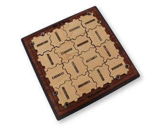 May include: A wooden puzzle game with a dark brown frame and light brown puzzle pieces. The pieces are engraved with binary numbers. The game is labeled "Bits & Bytes" and "Schesten-Spiele".