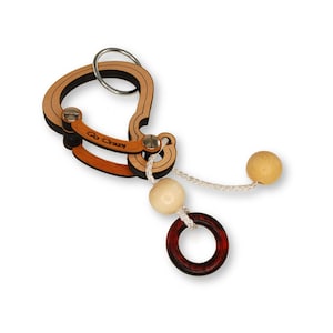 May include: Wooden puzzle with a light brown and dark brown design. The puzzle has a metal ring, a wooden ring, two wooden balls, and a dark red wooden ring. The text "Go Crazy" is visible on the puzzle.