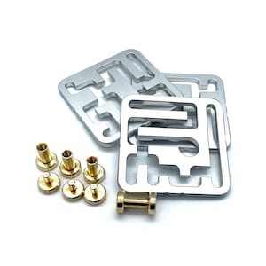 May include: A collection of silver metal square components with intricate cut-out designs, alongside several brass-colored cylindrical fasteners and a small brass dumbbell-shaped object. The items are arranged on a white surface.
