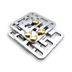 May include: A silver metal puzzle with a maze-like design. Four gold-colored circular pieces are placed on the puzzle's surface. The puzzle is square-shaped and appears to be made of multiple layers.
