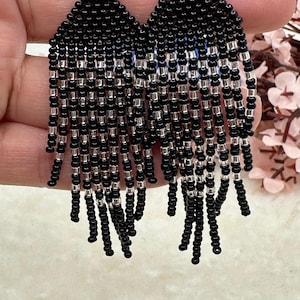 May include: Black and silver beaded fringe earrings. The earrings are triangular shaped and have a silver hook closure.