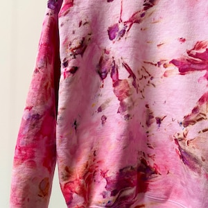 Op de afbeelding: Roze tie-dye sweatshirt met een wit label met daarop "Shop Dye".