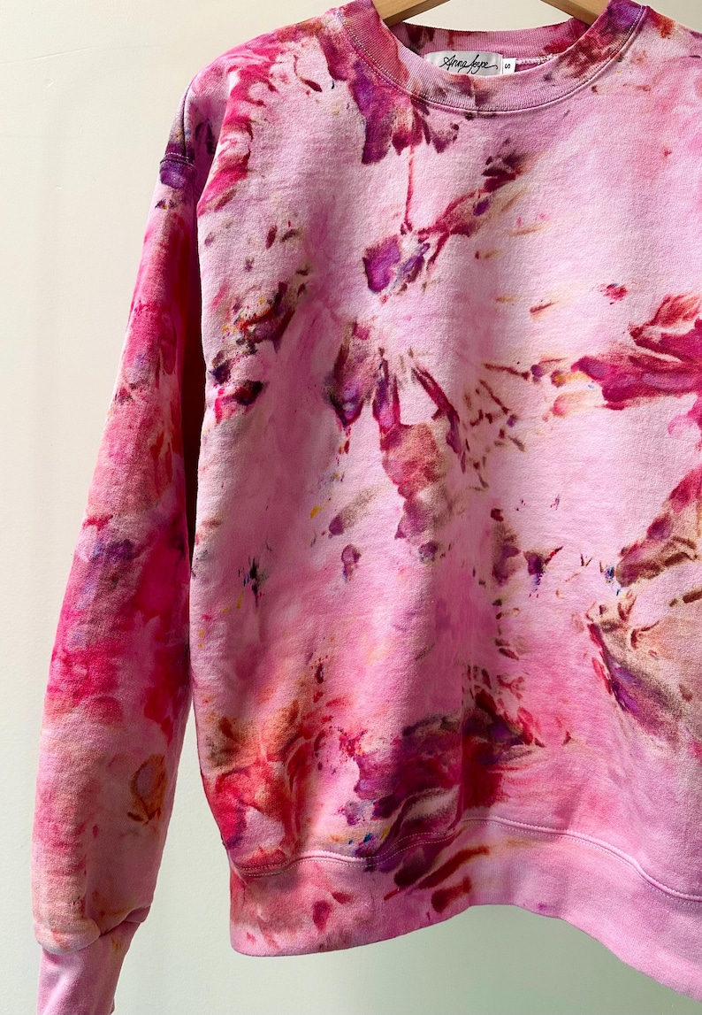 Op de afbeelding: Roze tie-dye sweatshirt met een wit label met daarop "Shop Dye".