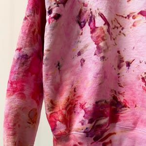 Op de afbeelding: Roze tie-dye sweatshirt met een losse pasvorm en lange mouwen. De sweatshirt heeft een uniek, abstract patroon met tinten roze, rood, paars en bruin.