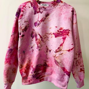 Op de afbeelding: Roze tie-dye sweatshirt met een lichtroze basis en donkerdere roze, paarse en oranje tie-dye patronen. De sweatshirt heeft een ronde hals en lange mouwen.