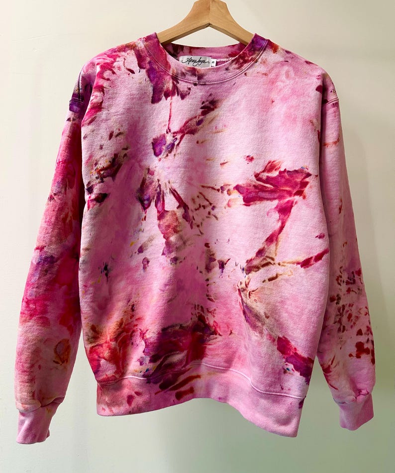 Op de afbeelding: Roze tie-dye sweatshirt met een lichtroze basis en donkerdere roze, paarse en oranje tie-dye patronen. De sweatshirt heeft een ronde hals en lange mouwen.