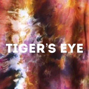 Może przedstawiać: Tkanina tie-dye z wirującym wzorem w kolorze pomarańczowym, czerwonym, fioletowym i czarnym. Na tkaninie nadrukowany jest biały napis "TIGER'S EYE".