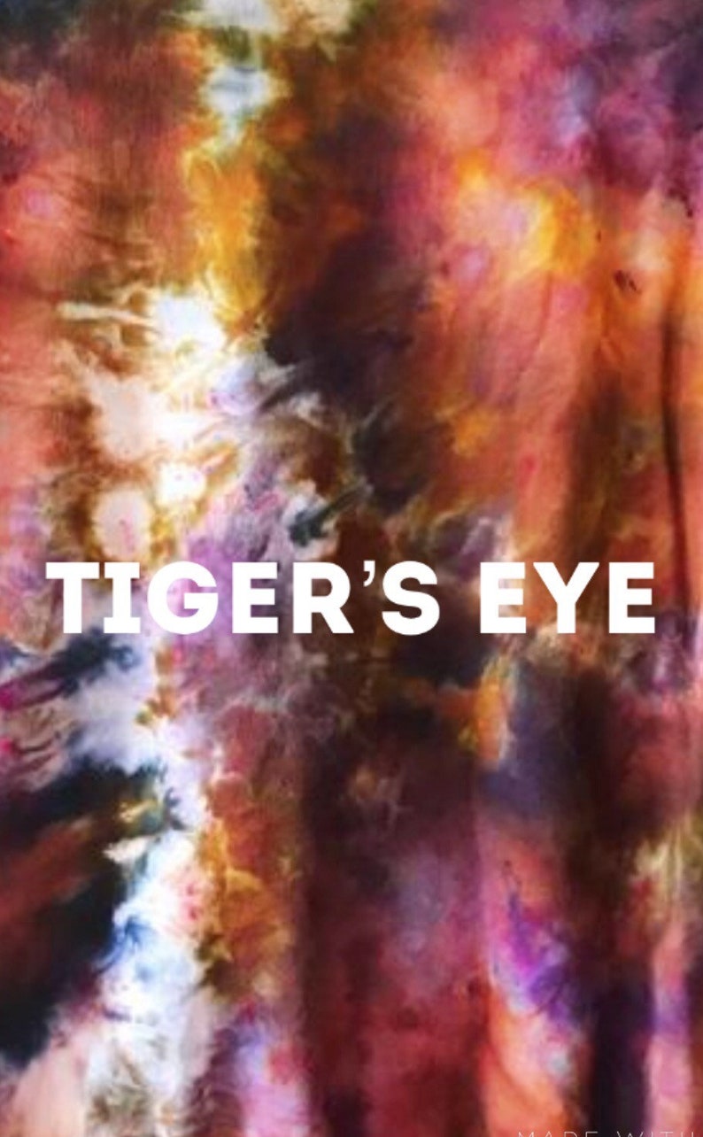 Może przedstawiać: Tkanina tie-dye z wirującym wzorem w kolorze pomarańczowym, czerwonym, fioletowym i czarnym. Na tkaninie nadrukowany jest biały napis "TIGER'S EYE".