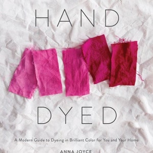 Może przedstawiać: Książka zatytułowana "HAND DYED" z podtytułem "A Modern Guide to Dyeing in Brilliant Color for You and Your Home" autorstwa Anny Joyce. Okładka przedstawia pr&oacute;bki tkaniny w kolorze r&oacute;żowym i czerwonym.