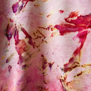 Op de afbeelding: Roze stof met een tie-dye patroon in tinten rood, paars en bruin.