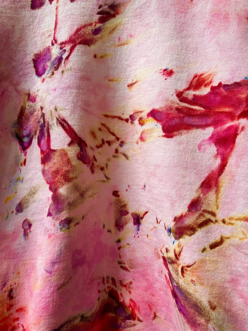 Op de afbeelding: Roze stof met een tie-dye patroon in tinten rood, paars en bruin.