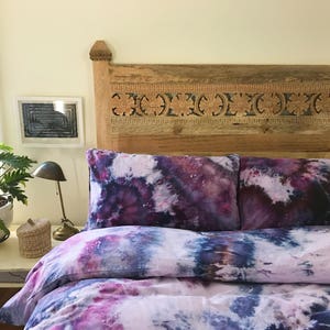 Könnte beinhalten: Ein Bett mit einem geschnitzten Holz-Kopfteil und einem Bettbezug und Kissenbezügen in Lila und Blau mit Batik-Muster.