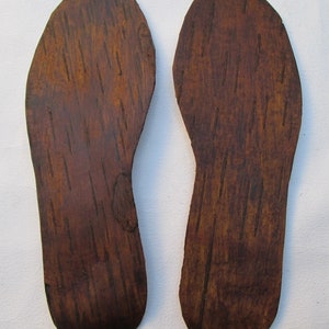 Puede incluir: Dos plantillas de madera marrón con un patrón de veta de madera. Las plantillas tienen forma de pies.