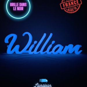May include: A glowing blue sign that spells "William" in a cursive font. The sign is illuminated against a dark background. The image also includes a "Made in France" stamp and text that reads "Brille dans le noir".