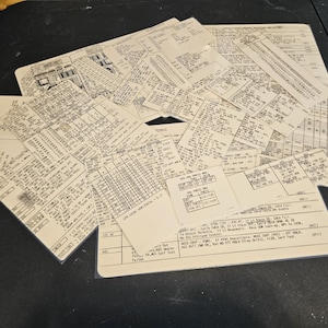 May include: A collection of vintage aviation documents, including flight logs and checklists, are arranged on a dark surface. The papers are filled with detailed text, tables, and diagrams, showcasing the technical aspects of flight operations.