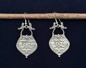May include: A pair of silver earrings with a heart-shaped design and intricate details. The earrings feature a small bird on each side of the heart.