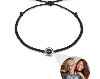 Peut inclure: Bracelet en cordon tressé noir avec une perle centrale argentée. La perle semble contenir une petite image. Un gros plan montre deux femmes souriantes, une plus âgée et une plus jeune.