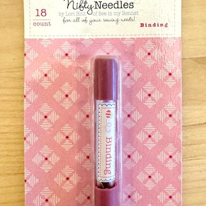 May include: A package of "Nifty Needles" binding needles. The pink packaging has a diamond pattern with red dots. The package includes a cylindrical needle container with the word "Binding" on it. The package reads "18 count".