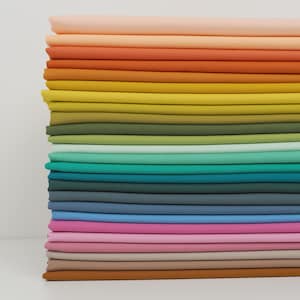 K&ouml;nnte beinhalten: Ein Stapel farbenfroher Stoffmuster in einem Farbverlauf. Die Farben reichen von Pfirsich und Orange oben, &uuml;ber Gelb-, Gr&uuml;n-, Blau- und Rosat&ouml;ne bis hin zu einem braunen Muster unten. Der Stoff scheint ein glattes, einfarbiges Material zu sein.
