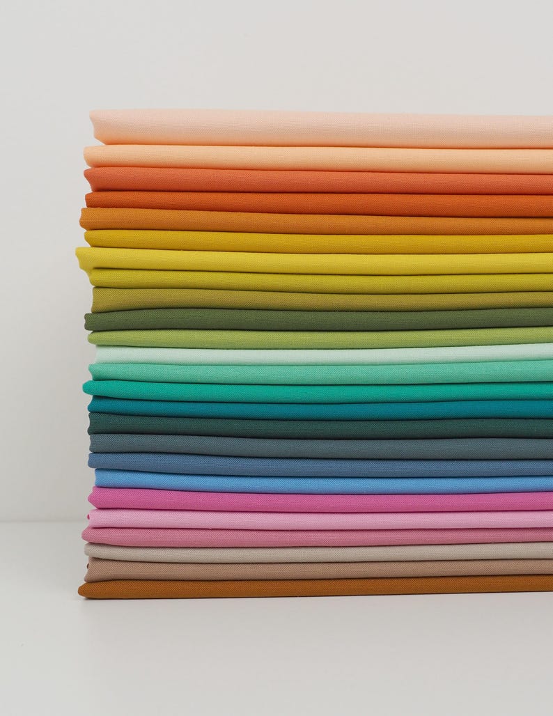 K&ouml;nnte beinhalten: Ein Stapel farbenfroher Stoffmuster in einem Farbverlauf. Die Farben reichen von Pfirsich und Orange oben, &uuml;ber Gelb-, Gr&uuml;n-, Blau- und Rosat&ouml;ne bis hin zu einem braunen Muster unten. Der Stoff scheint ein glattes, einfarbiges Material zu sein.