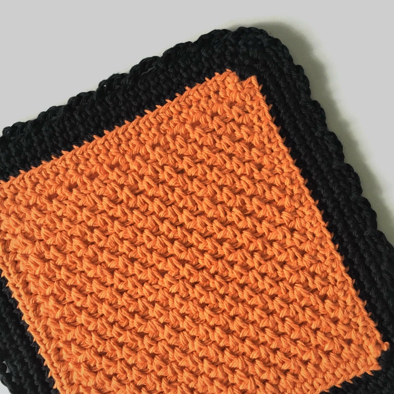May include: Orange crochet dishcloth with a black crocheted border.
