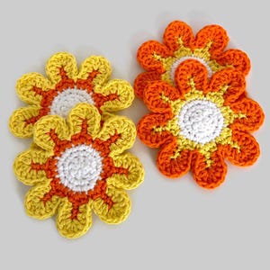 May include: Three crocheted flower coasters in yellow, orange, and white. The coasters are shaped like daisies with a white center and alternating yellow and orange petals.