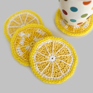 May include: Four crocheted lemon-shaped coasters in yellow and white. The coasters are made with a textured yarn and have a raised design that resembles a lemon slice.