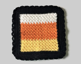 May include: A crocheted candy corn square with a black border. The candy corn is made of white, orange, and yellow yarn.