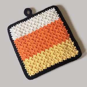 May include: A crocheted pot holder in the shape of a candy corn. The pot holder is made with black, white, orange, and yellow yarn. It has a loop handle for hanging.