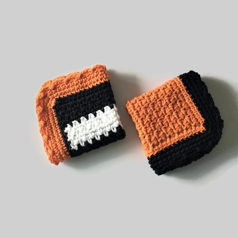May include: Two crocheted dishcloths in orange, black, and white. One dishcloth has a white stripe with a scalloped edge.