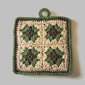 May include: A square, handmade crochet potholder with a loop for hanging. The design features four squares with a floral pattern in shades of green, brown, and cream, outlined with a dark green border. The potholder is made of yarn.
